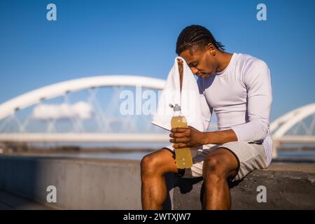 Portrait d'un jeune homme afro-américain fatigué qui essuie la sueur de son visage après le jogging. Banque D'Images