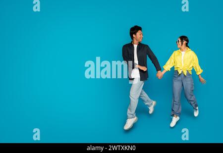 Couple joyeux se tenant la main et dansant, avec l'homme dans une veste marine et une femme portant des lunettes de soleil Banque D'Images
