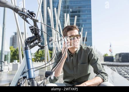 jeune homme d'affaires fait du vélo électrique sur son chemin vers la tour où se trouve son bureau, souriant et riant Banque D'Images