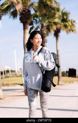 femme asiatique dans la marche de sportswear avec tapis de yoga Banque D'Images