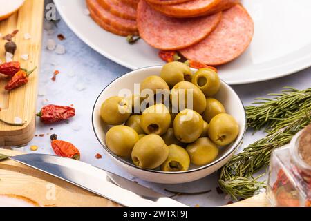 olives vertes dans un bol sur la table entourées de produits tels que saucisses, bacon et épices Banque D'Images