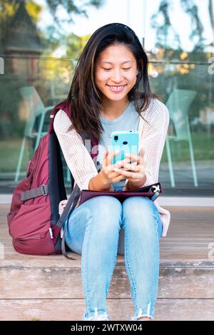 jeune femme asiatique assise naviguant sur internet sur le téléphone portable à l'extérieur. Vertical Banque D'Images