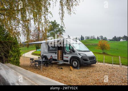 Camping-car ou camping-car garé dans la nature de la campagne. Femme boit du café devant le camping-car camping-car camping-car, garé sous les arbres quand ex Banque D'Images