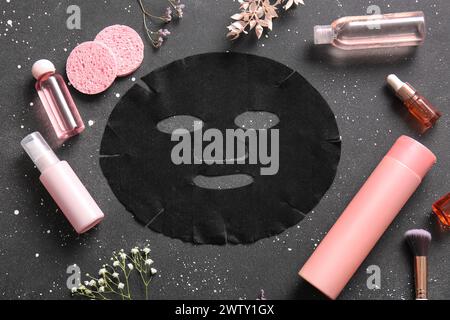 Masque de drap facial avec différents produits cosmétiques et fleurs de gypsophila sur fond noir Banque D'Images