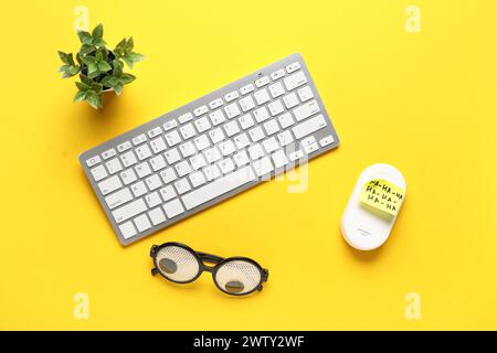 Lunettes drôles, note collante, clavier d'ordinateur et souris sur fond jaune. Farce du jour des fous d'avril Banque D'Images