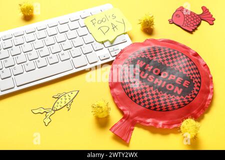 Clavier d'ordinateur, note collante et coussin whoopee sur fond jaune. Farce du jour des fous d'avril Banque D'Images