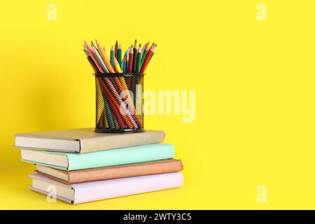 Porte-crayon plein de crayons colorés et de livres sur fond jaune. Fin de l'école Banque D'Images