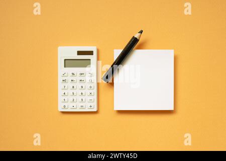 Fournitures de bureau. Calculatrice, bloc-notes, crayon sur fond de bureau orange. pose à plat, vue de dessus, espace de copie Banque D'Images