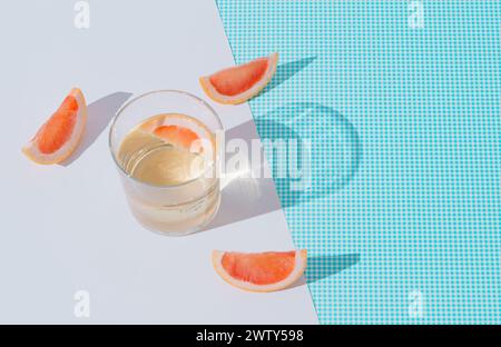 Scène d'été faite avec une boisson rafraîchissante avec des tranches de pamplemousse frais sur fond blanc et bleu. Soleil et ombres. Concept de cocktail minimal. Banque D'Images