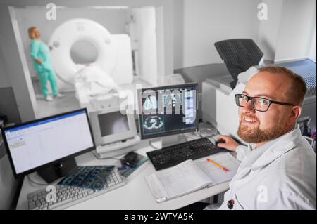Tomodensitométrie médicale ou scanner IRM. Docteur souriant à la caméra, infirmière faisant IRM. Spécialistes travaillant à l'hôpital, examen médical, étude des résultats sur ordinateur. Concept de diagnostic moderne. Banque D'Images