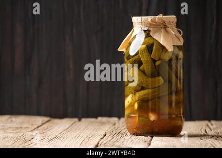 Concombres marinés dans un bocal en verre fermé sur une surface en bois avec de l'espace pour le texte. Concombres en conserve faits maison dans une bouteille, espace de copie. Banque D'Images