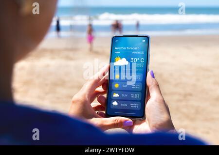 Femme à l'extérieur sur la plage en vérifiant les prévisions météorologiques sur une application sur son téléphone portable. Banque D'Images