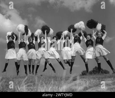 Neuf cheerleaders portant tous la même tenue, jupe blanche, top sombre avec la lettre 'O' dessus, tous sautant dans le temps en faisant un acclamé Banque D'Images