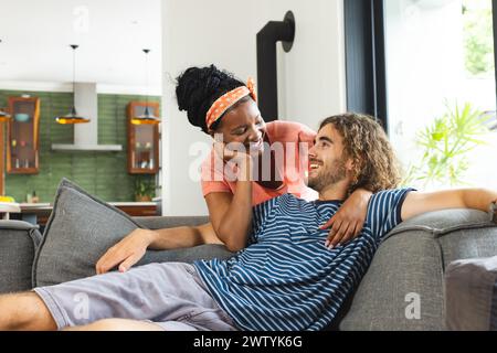 Un couple diversifié se détend sur un canapé gris à la maison, partageant un moment Banque D'Images