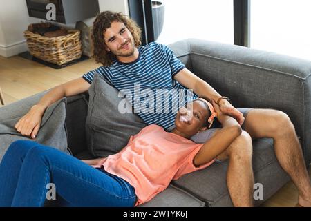 Un couple diversifié se détend confortablement sur un canapé gris à la maison Banque D'Images