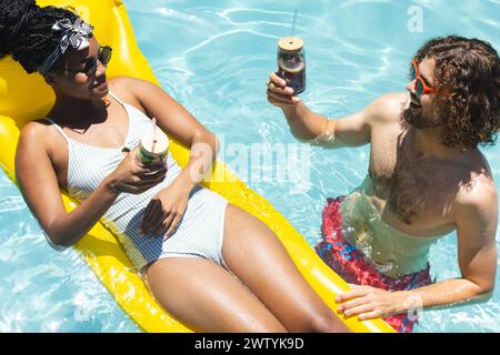 Un couple diversifié aime boire dans la piscine Banque D'Images