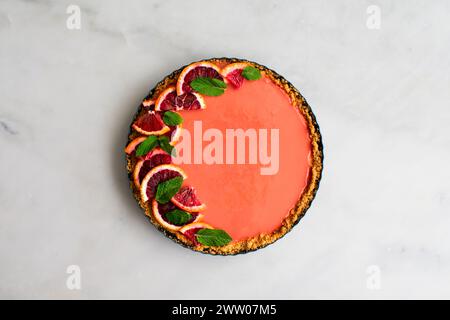 Tarte au cheesecake à l'orange sanguine sur une table en marbre blanc : tarte au cheesecake au caillé à l'orange framboise garnie de feuilles de menthe dans une croûte de craquelins graham Banque D'Images