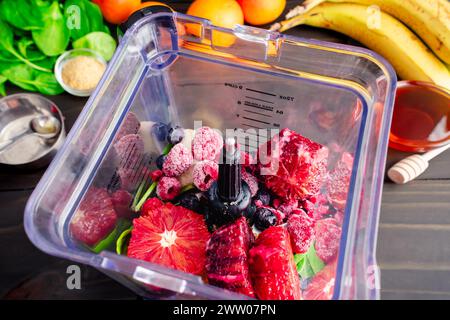 Vue de dessus du Smoothie à l'orange sanguine mélangée dans un mélangeur : fruits frais et congelés non mélangés, jeunes feuilles d'épinards, graines de lin dorées et miel Banque D'Images