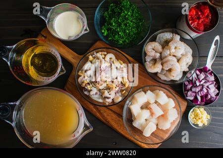 Ingrédients de la soupe de fruits de mer préparée et décongelée sur la planche à découper : poisson haché et mesuré, crevettes, oignons, persil et autres ingrédients sur une table en bois Banque D'Images