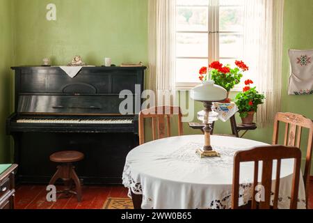 Intérieur de salon vintage avec une table ronde et un piano noir, lumière du jour lumineuse venant par la fenêtre. Banque D'Images