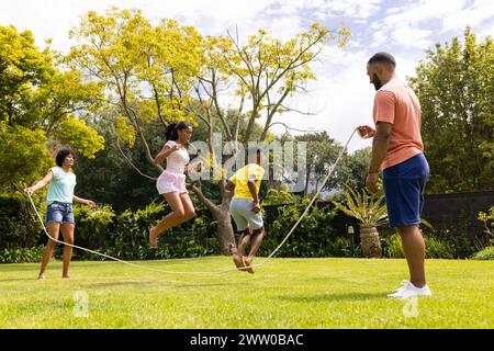 Une famille afro-américaine aime sauter à la corde ensemble dans un jardin luxuriant Banque D'Images