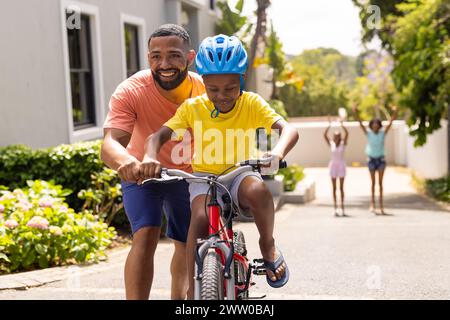 Père afro-américain apprend à son fils à faire du vélo à l'extérieur de la maison Banque D'Images