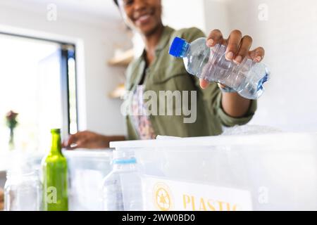 Une jeune femme afro-américaine trie les plastiques dans un bac de recyclage à la maison dans la cuisine Banque D'Images