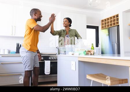 Un couple diversifié recyclant ensemble dans une cuisine avec un high-cinq à la maison Banque D'Images