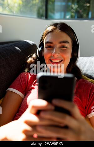 Une jeune femme brune caucasienne s'engage avec son smartphone sur le canapé à la maison Banque D'Images