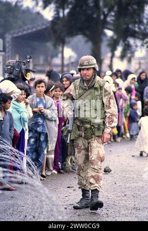 Première Guerre du Golfe : 23 mars 1991 Un soldat de l'armée américaine de la 3ème division blindée 'fer de lance' garde une ligne ordonnée d'Irakiens déplacés, faisant la queue pour de la nourriture et des boissons près de Safwan dans le sud de l'Irak. Banque D'Images