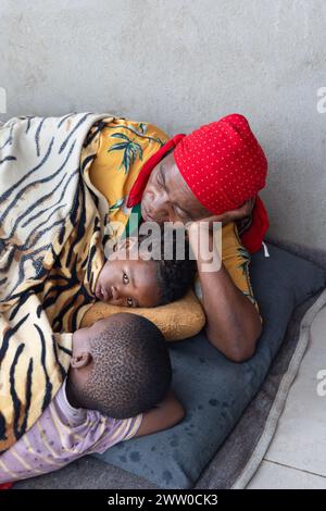 femme africaine du village assise sur le sol avec deux enfants couverts dans une couverture Banque D'Images