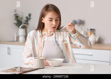 Belle femme mangeant de la soupe avec une cuillère à la table dans la cuisine Banque D'Images