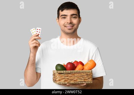Jeune homme avec des ampoules de pilules de vitamine A et de la nourriture saine sur fond clair Banque D'Images