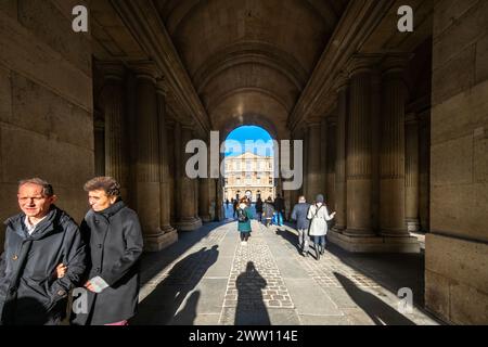 Visiteurs marchant à travers l'entrée sud ensoleillée de la Cour carrée du Louvre à Paris. Banque D'Images