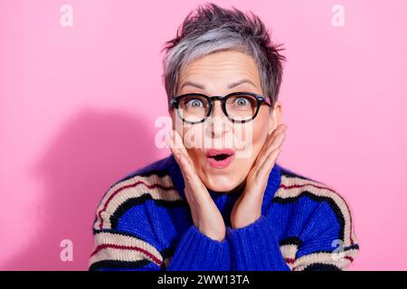 Portrait de femme extatique ravie porter un pull rayé dans des mains de lunettes sur les joues étonné regardant isolé sur fond de couleur rose Banque D'Images