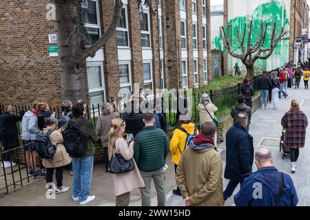 Londres, Royaume-Uni. 19 mars 2024. Les membres du public admirent et prennent des photos de nouvelles œuvres d'art du Street artiste de renommée mondiale Banksy qui étaient apparues la veille sur le côté d'un immeuble résidentiel derrière un arbre situé dans le jardin d'un bloc de logements sociaux à Finsbury Park. L'œuvre d'art, revendiquée par l'artiste de rue, prend la forme d'une peinture verte pulvérisée sur un mur derrière un cerisier pollardé de manière à apparaître comme du feuillage lorsqu'on la regarde de face, avec un pochoir d'une femme tenant une laveuse haute pression. La nuance de peinture verte utilisée semble correspondre à celle utilisée par Islington Banque D'Images