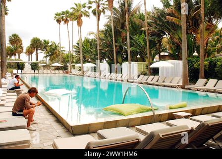 Un jeune homme se repose dans une piscine extérieure entourée de palmiers dans un complexe de Miami Beach, en Floride Banque D'Images