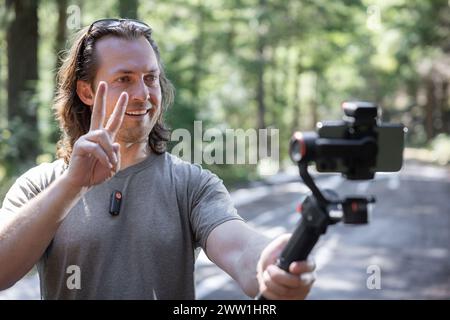 Créateur de contenu utilisant. un cardan de téléphone pour filmer dans la nature avec une forêt floue en arrière-plan Banque D'Images