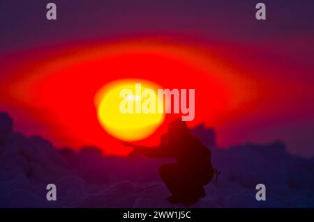 Inupiaq homme tient sa main sous le soleil de minuit dans la mer des Tchouktches, au large du village arctique de Barrow, Alaska Banque D'Images