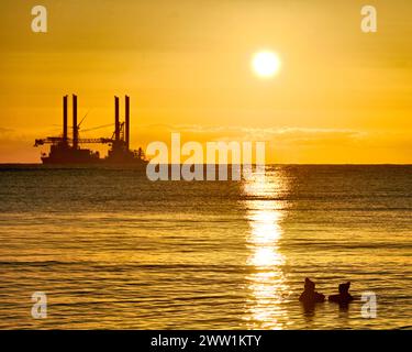 Deux femmes nageuses sauvages discutant à l'aube dans la mer du Nord avec un ciel de soleil doré et des reflets de mer Banque D'Images