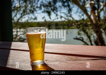 Une bière fraîche sur un rebord en bois avec un fond de rivière. Banque D'Images