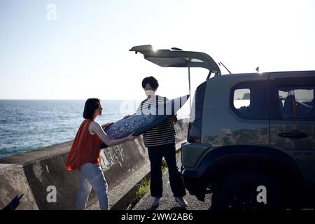 Un homme et une femme debout à côté d'une voiture avec une planche de surf Banque D'Images