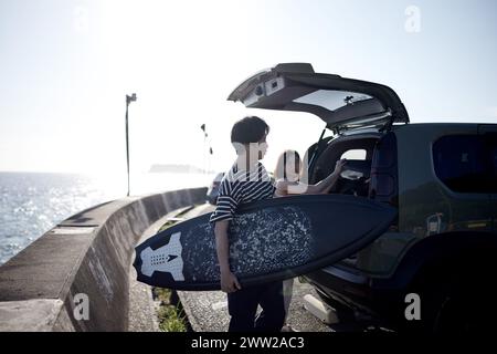 Un homme et une femme debout à côté d'une voiture avec une planche de surf Banque D'Images