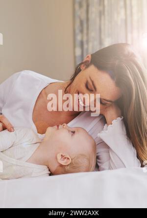 Mère, ludique et soin avec bébé sur le lit pour se lier, l'amour et se détendre ensemble dans la chambre. Lumière parasite, femme heureuse et fille pour l'enfance Banque D'Images