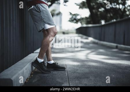 Un homme se tient sur la passerelle après avoir couru dans le parc du centre-ville avant l'entraînement cardio. Santé et style de vie dans le concept de vie de grande ville. Banque D'Images