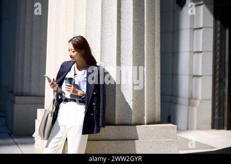 Une femme en costume tenant un café et regardant son téléphone Banque D'Images