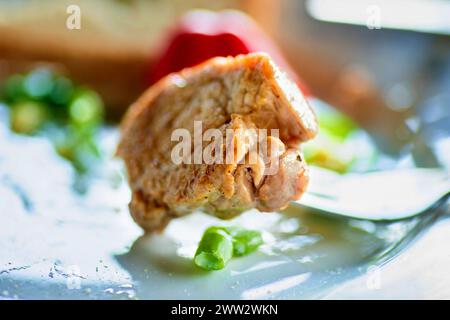 Morceau de steak broché sur la fourchette, poivron rouge, jeunes pousses d'oignon vert sur l'assiette, gros plan. Banque D'Images