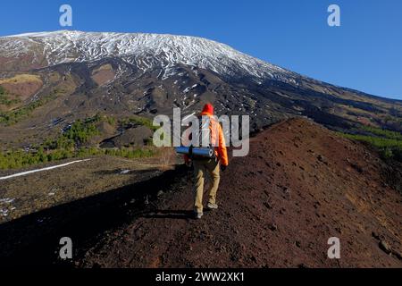 Randonneur de vue arrière avec sac à dos marche le long de la crête du cratère du volcan éteint dans Etna Park, sur fond de neige et pente raide du sud-ouest Banque D'Images