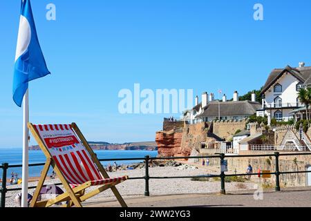 Vue sur les maisons traditionnelles au toit de chaume surplombant la plage à l'extrémité ouest de la ville avec un grand transat au premier plan, Sidmouth, Devon, Royaume-Uni. Banque D'Images