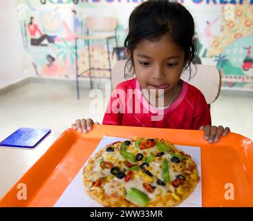 Une jeune étudiante thaïlandaise sourit avec plaisir en mangeant une pizza pendant les cours Banque D'Images